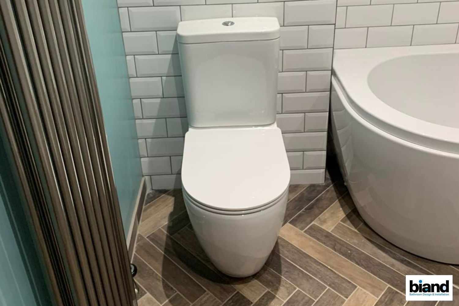 White toilet in a bathroom with tiled walls, patterned floor, and a tub visible on the right.