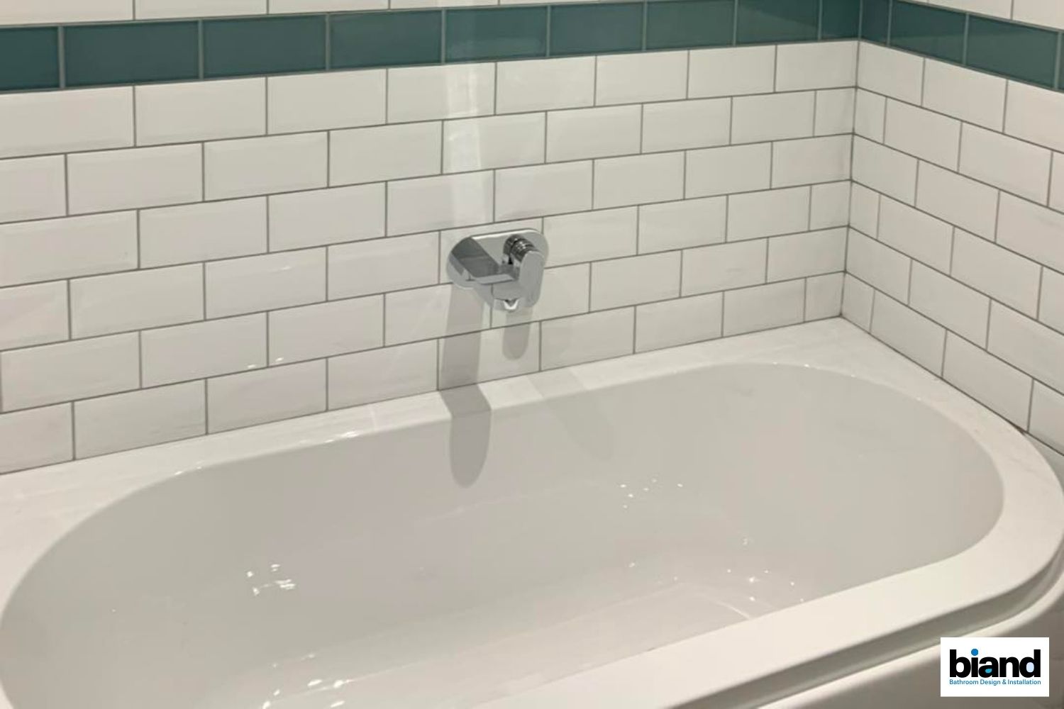 White bathtub with chrome faucet, white subway tile walls with teal accent, clean interior.