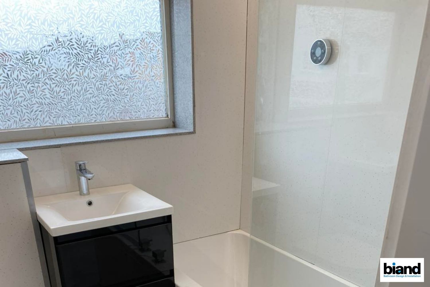 Small bathroom with black vanity, white shower/tub, frosted window.
