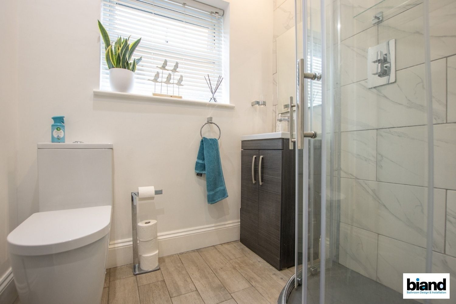 Bathroom with toilet, sink, and glass shower, natural light from a window.