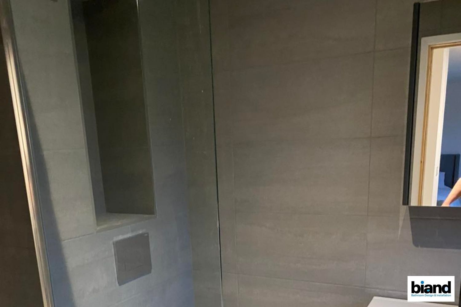 Gray tiled bathroom with a recessed shelf, a mirror, and a vertical seam.