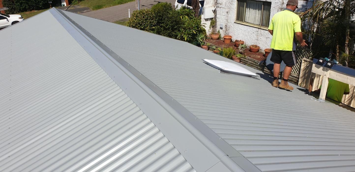 A Man is Standing on Top of a Metal Roof — Coast Metal Roof & Gutter In Tumbi Umbi, NSW