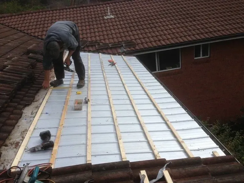 A Man is Installing a Skylight on the Roof of a Building — Coast Metal Roof & Gutter In Tumbi Umbi, NSW
