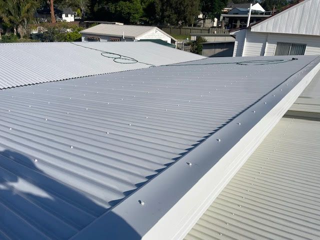 A Ladder is Sitting on the Roof of a House — Coast Metal Roof & Gutter In Tumbi Umbi, NSW