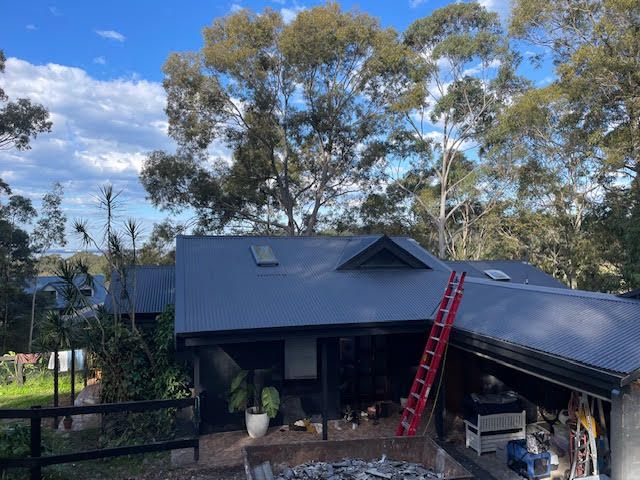 A Construction Worker is Working on the Roof of a Building — Coast Metal Roof & Gutter In Tumbi Umbi, NSW