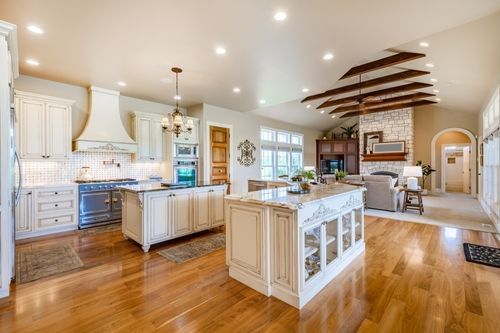 Bright, spacious kitchen with white cabinets, island, hardwood floors, and open living area with exposed beams