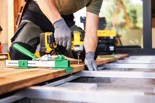 Person using a yellow power drill to assemble a wooden frame on a workbench