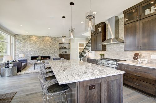 Modern kitchen with large marble island, dark wood cabinets, pendant lights, and open living area