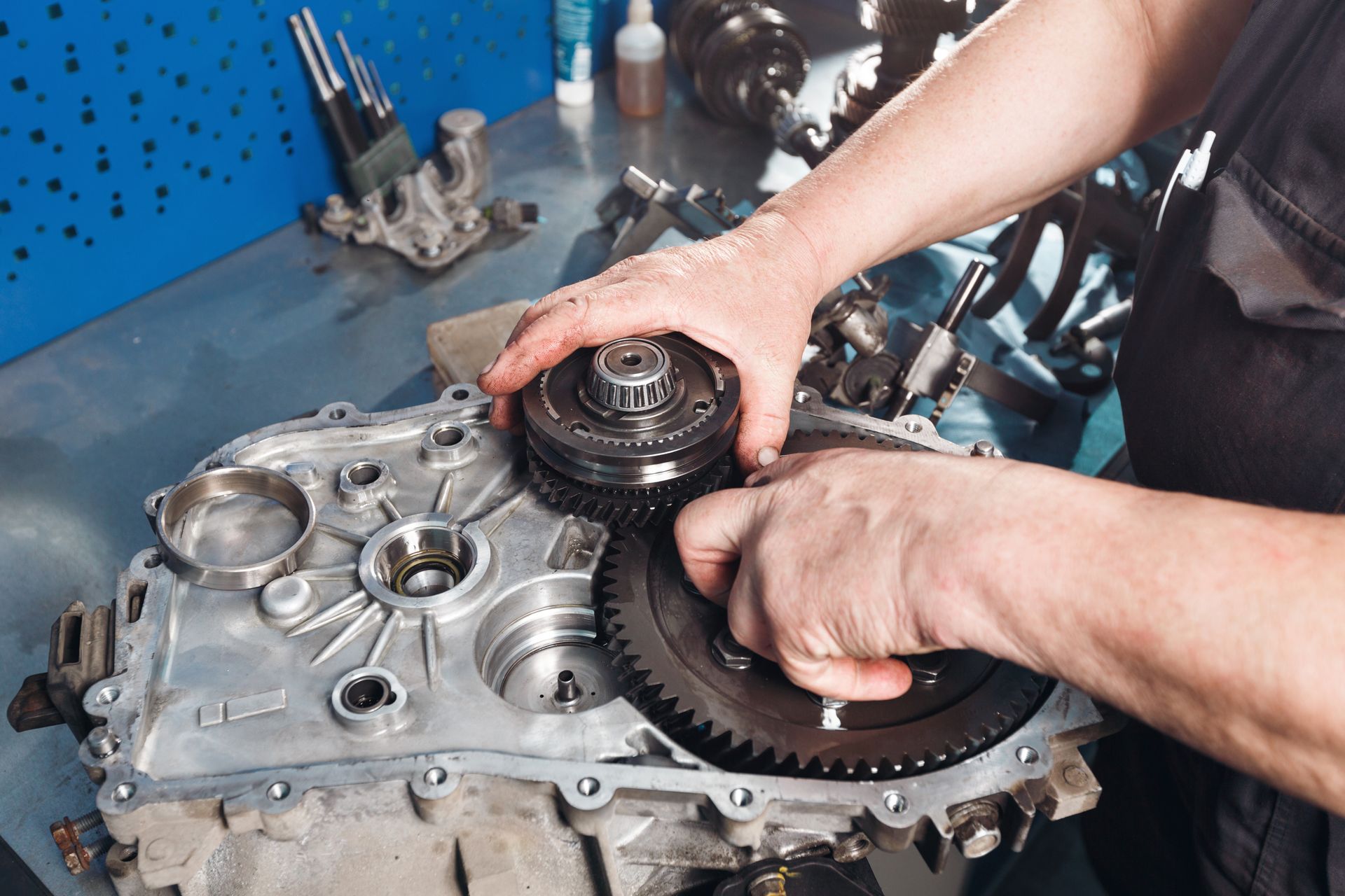 Hands assembling gears inside a metal gearbox on a workbench in a workshop