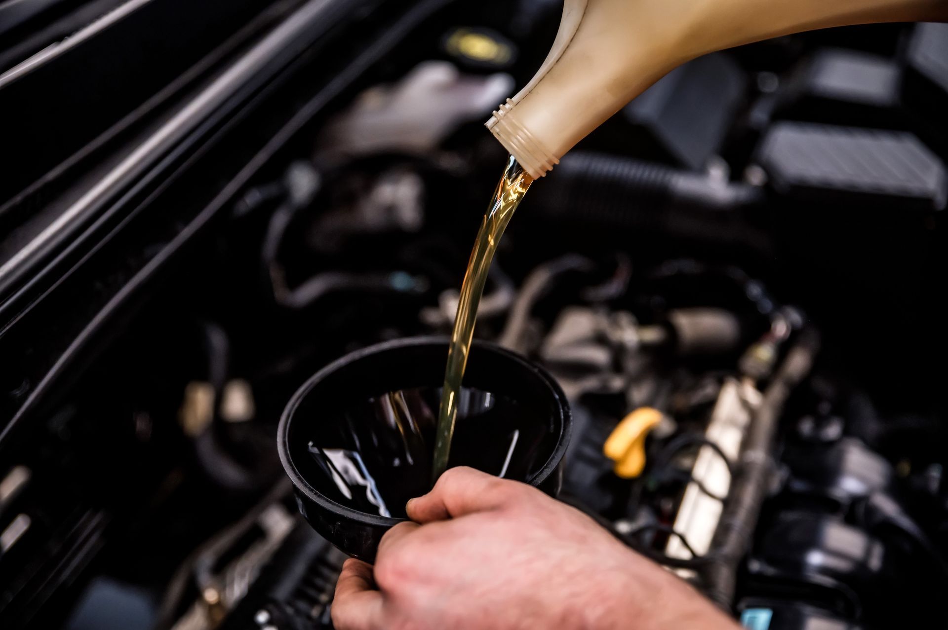 Oil being poured into a car engine with a funnel in the engine bay