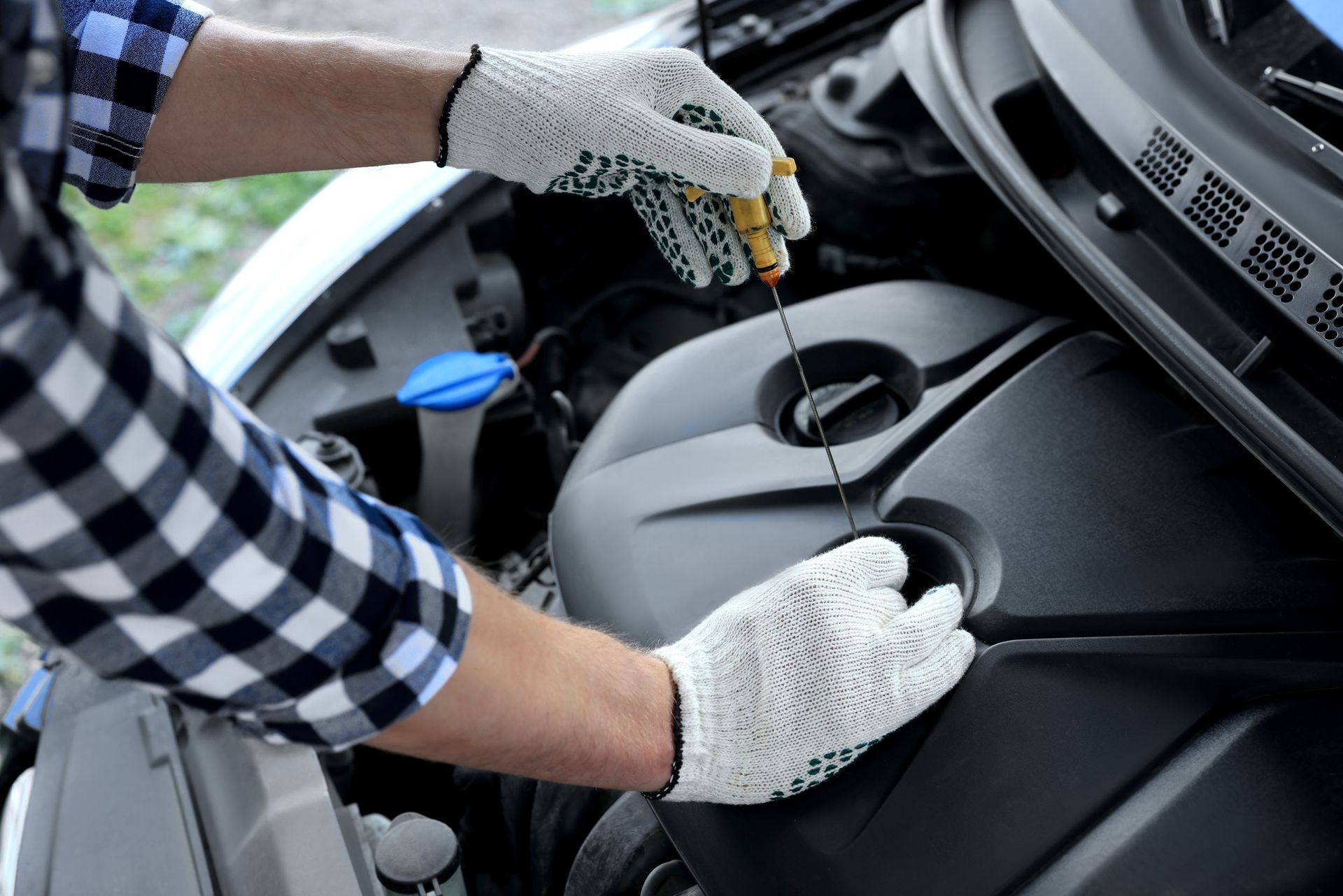 Gloved hands checking engine oil under a car hood with a dipstick