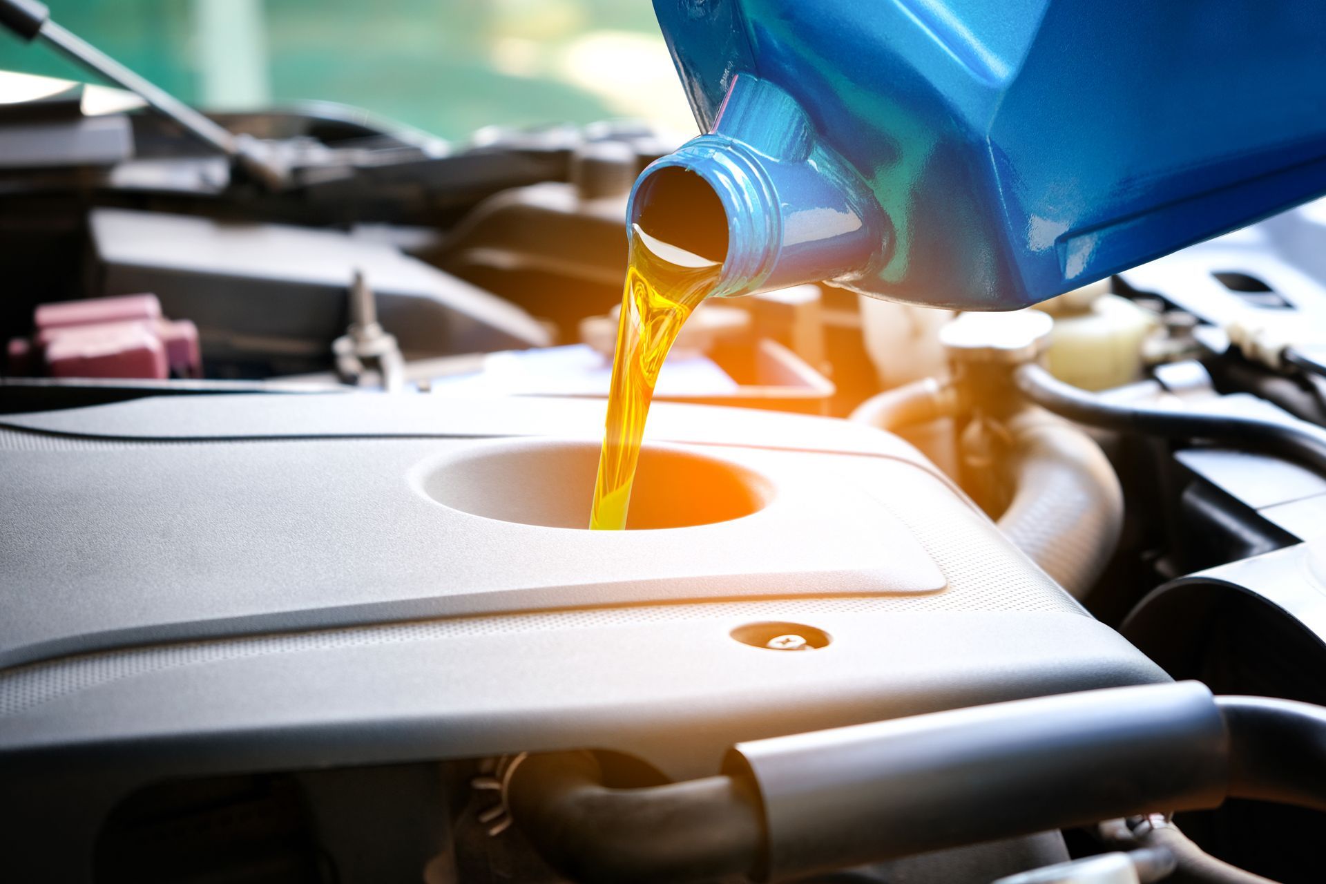Motor oil being poured from a blue container into an engine fill opening