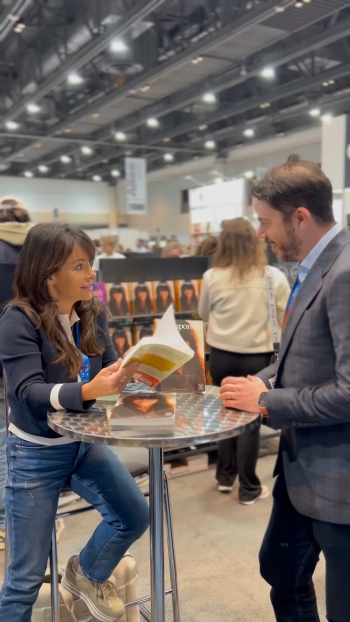 Deux personnes discutent sur un stand d'exposition professionnelle, l'une d'elles tenant une brochure jaune.