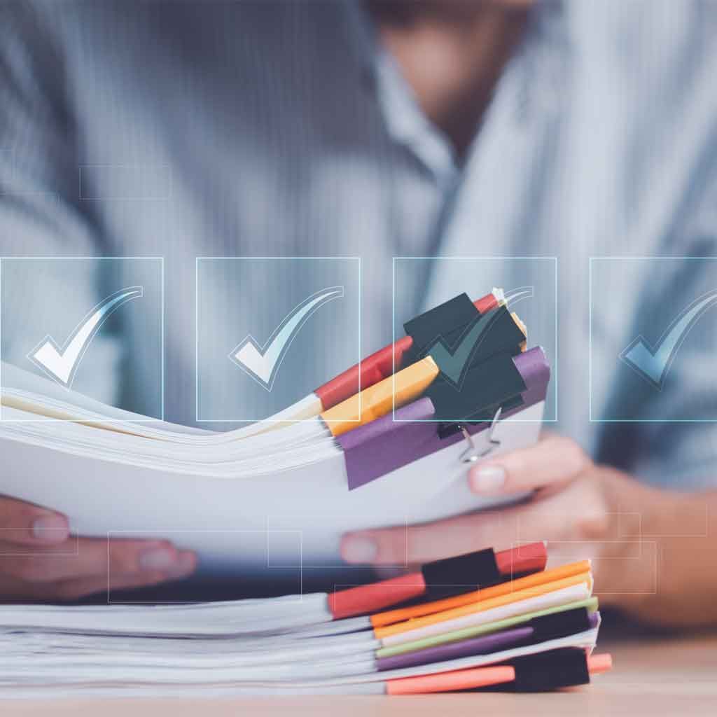 Person holding a stack of papers with colorful tabs, checkmarks overlayed.