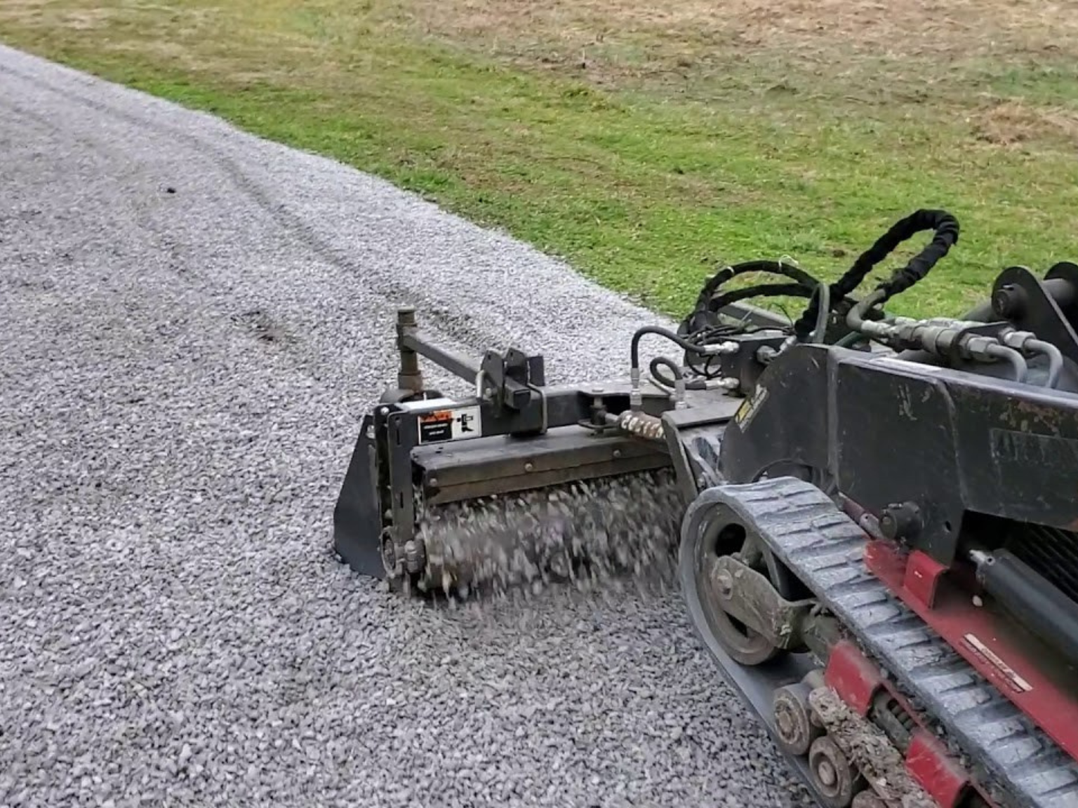 A track loader spreads and levels fresh gravel on a residential driveway in Bettendorf, Iowa.