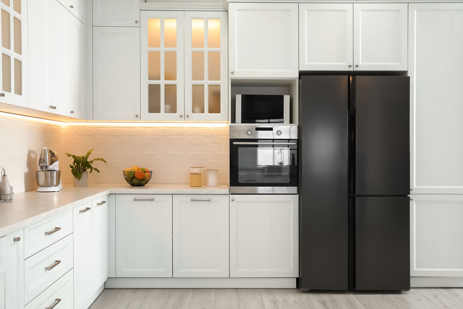 Modern white kitchen with black refrigerator, built-in oven, and warm under-cabinet lighting