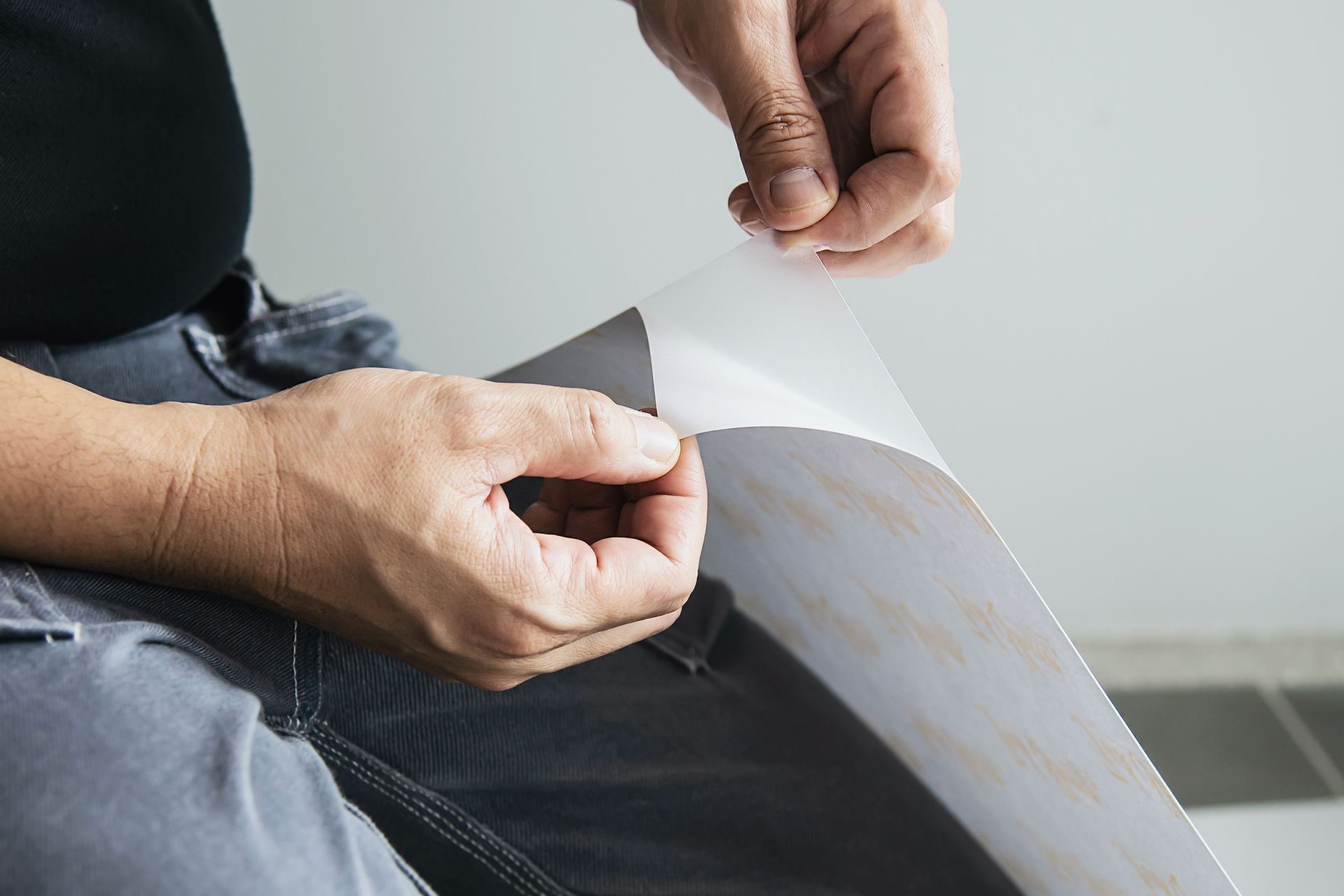 Hands holding and peeling a white adhesive sheet from black pants while seated