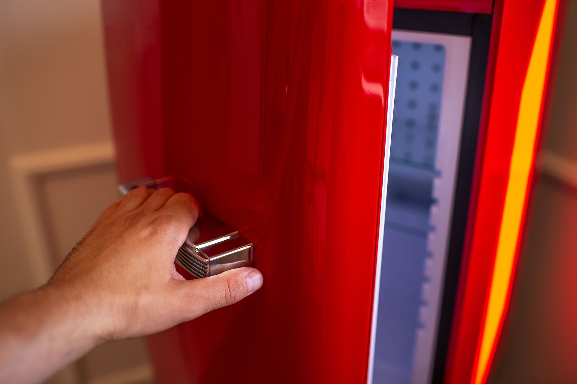 Hand opening a red refrigerator door, revealing a lit interior.