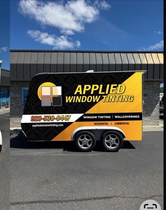 Yellow-and-black Applied Window Tinting trailer parked outside under a blue sky