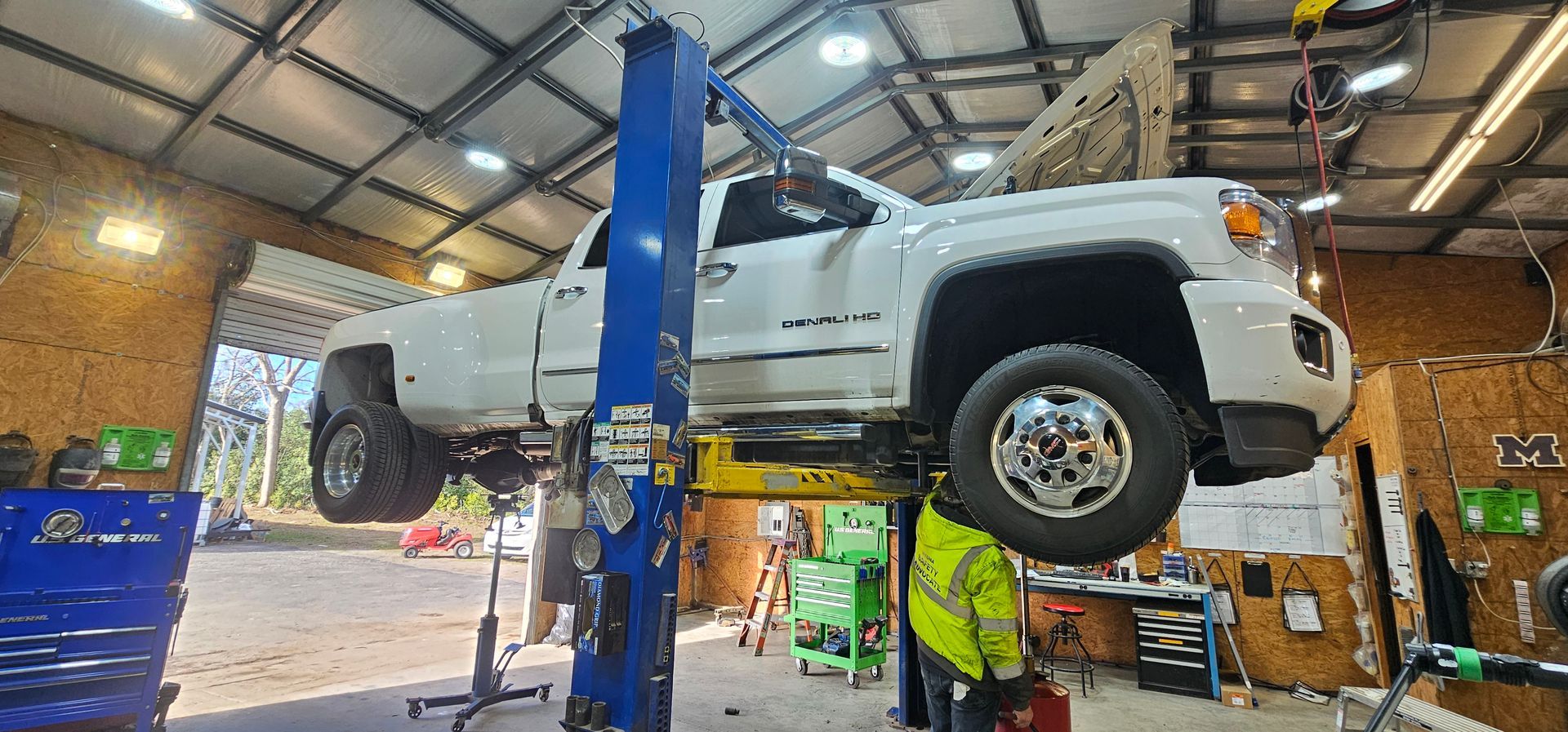 White SUV on a blue lift in an auto repair shop with two mechanics below | Masters Auto Group