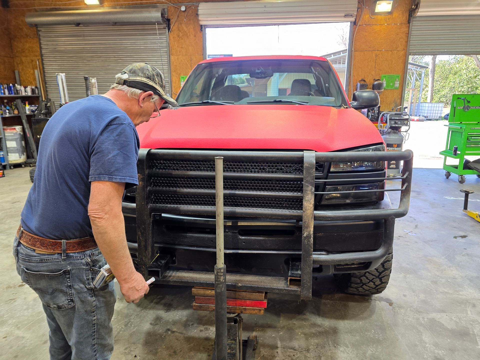 Man in blue shirt positioning a tow bar on a red pickup truck inside a garage | Masters Auto Group