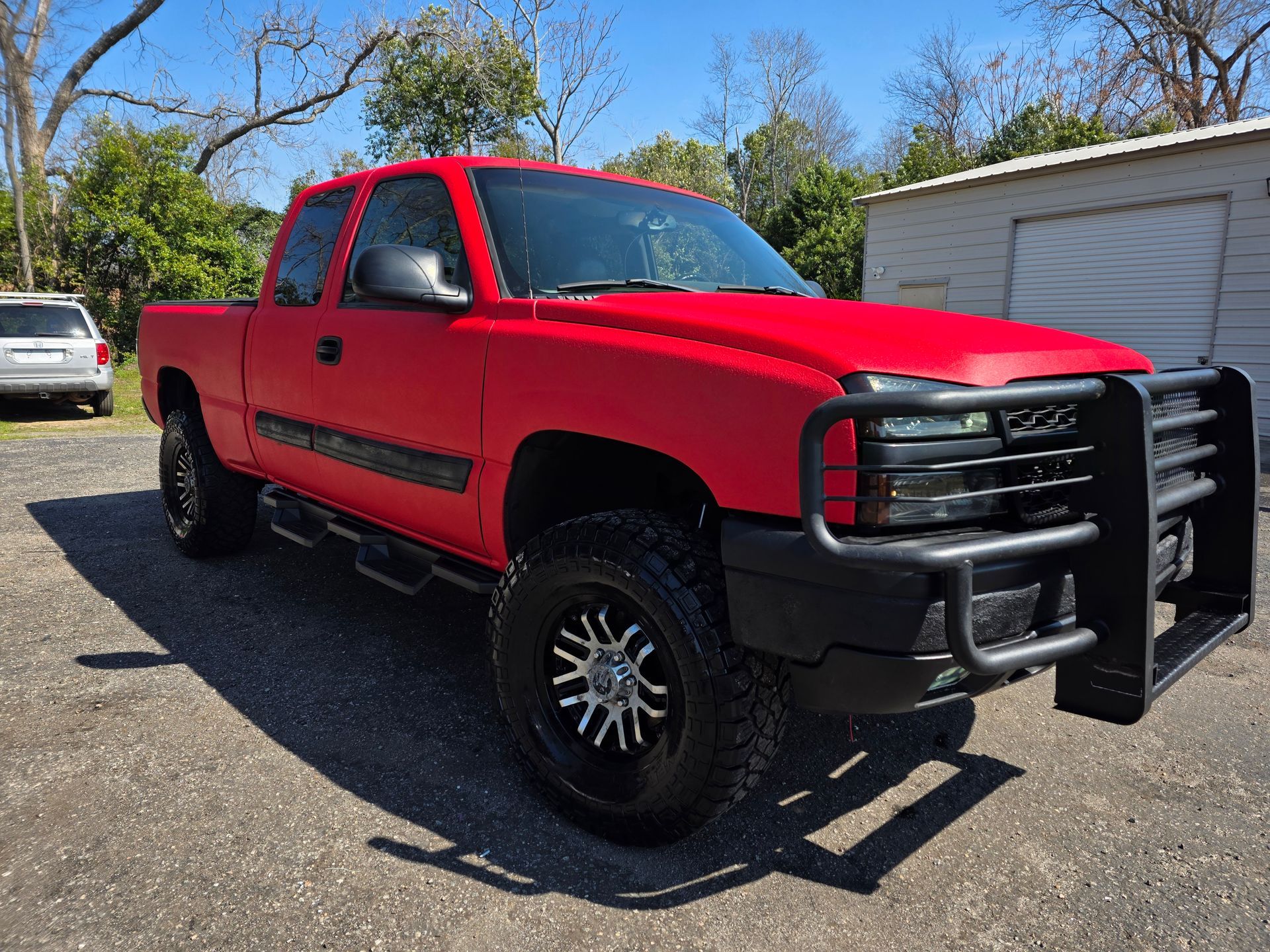 Red lifted pickup truck with black grille guard parked on a driveway outdoors. | Masters Auto Group