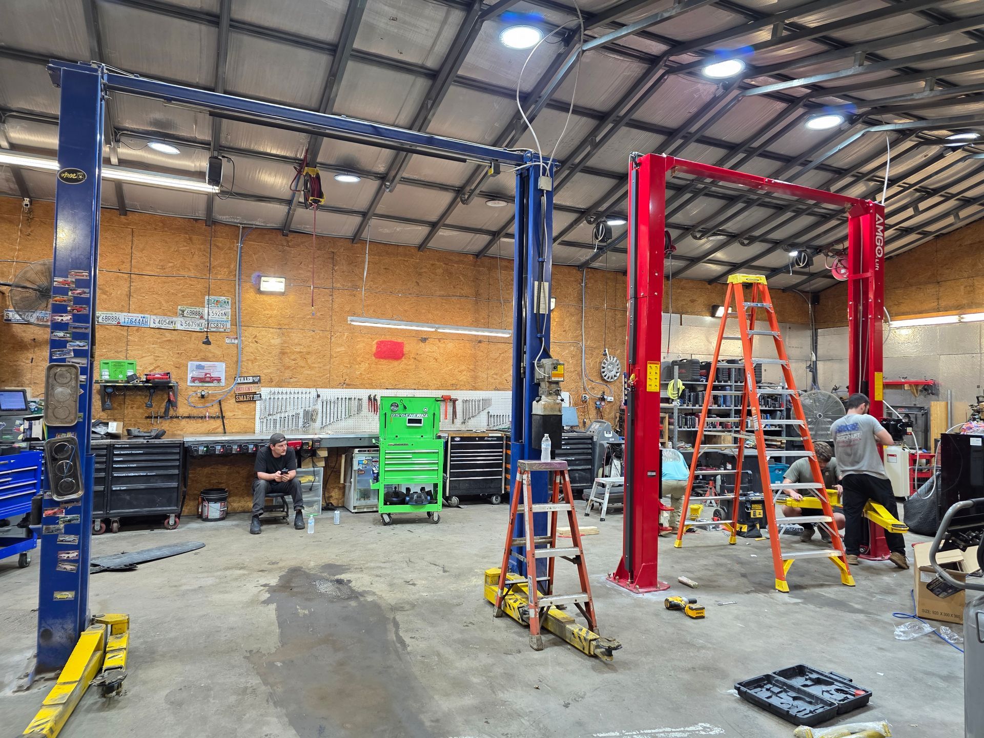 Warehouse workshop with two red vehicle lifts, ladders, tools, and equipment on a concrete floor | Masters Auto Group