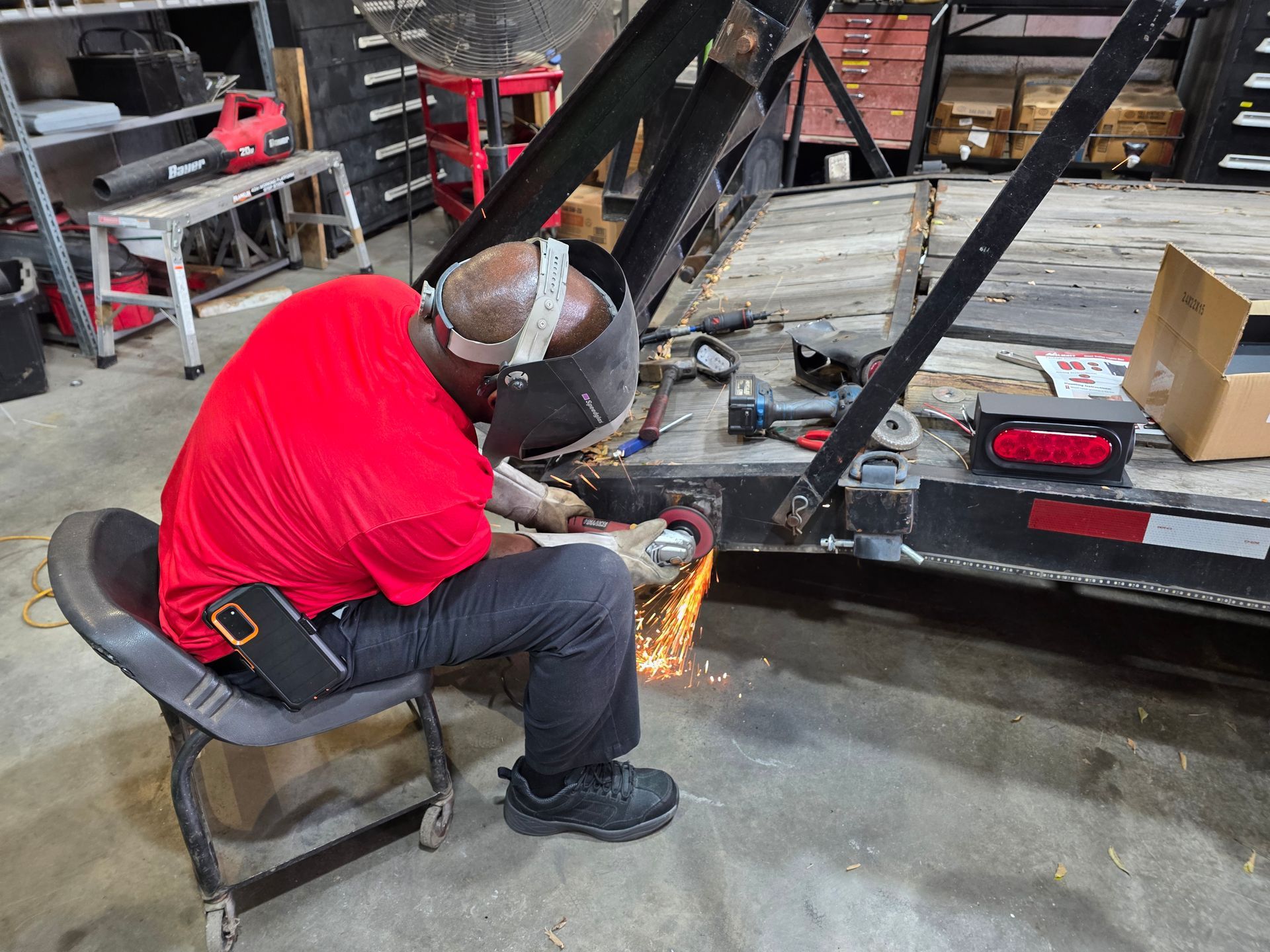 Worker in red shirt welding a metal frame in a workshop, with sparks flying. | Masters Auto Group