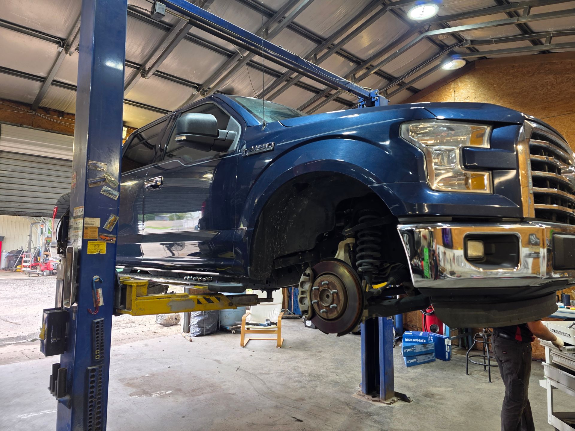 Blue pickup truck on a lift in an auto repair garage, with a wheel removed | Masters Auto Group