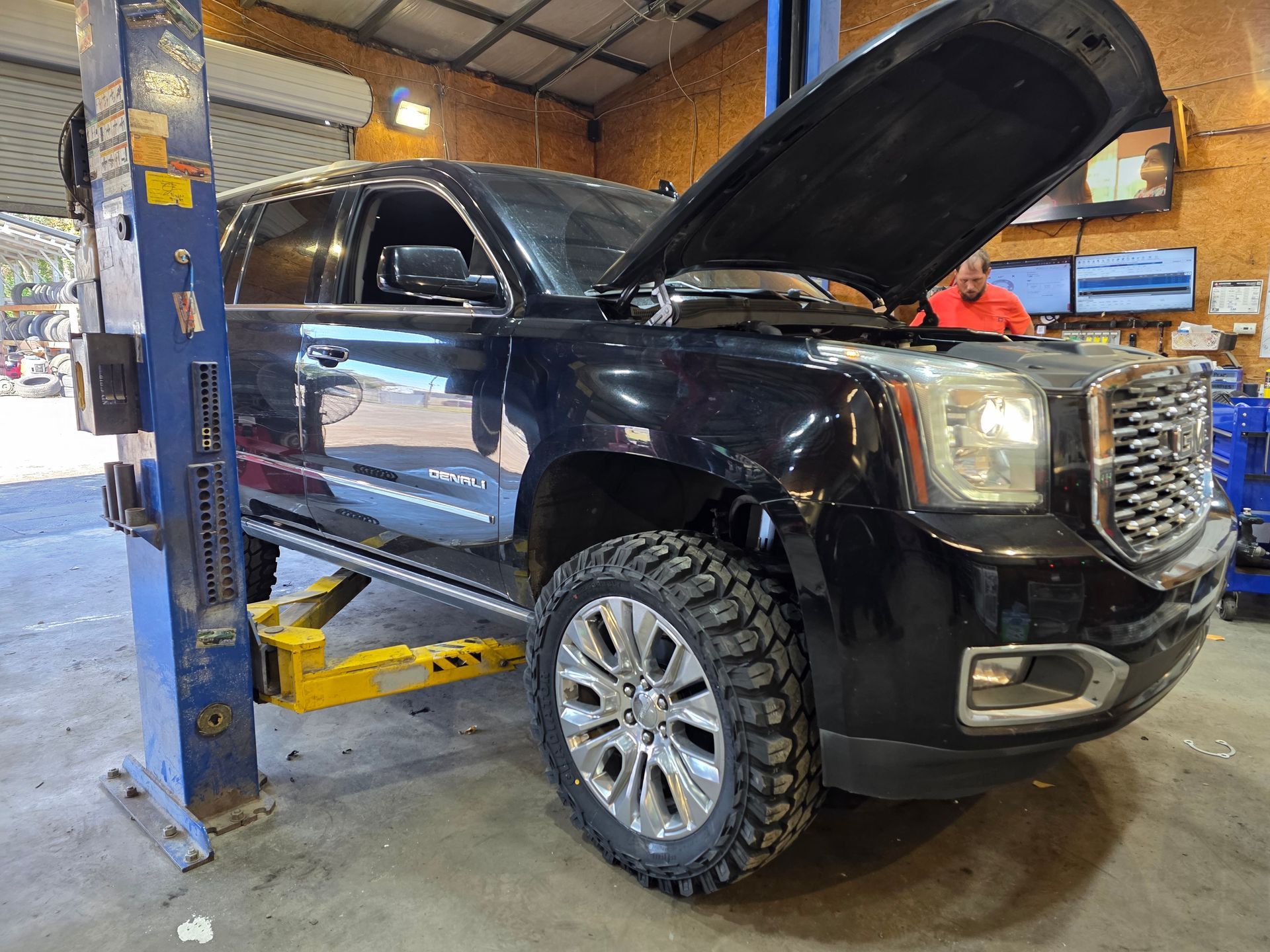 Black SUV lifted in an auto shop with hood open and front wheel removed. | Masters Auto Group