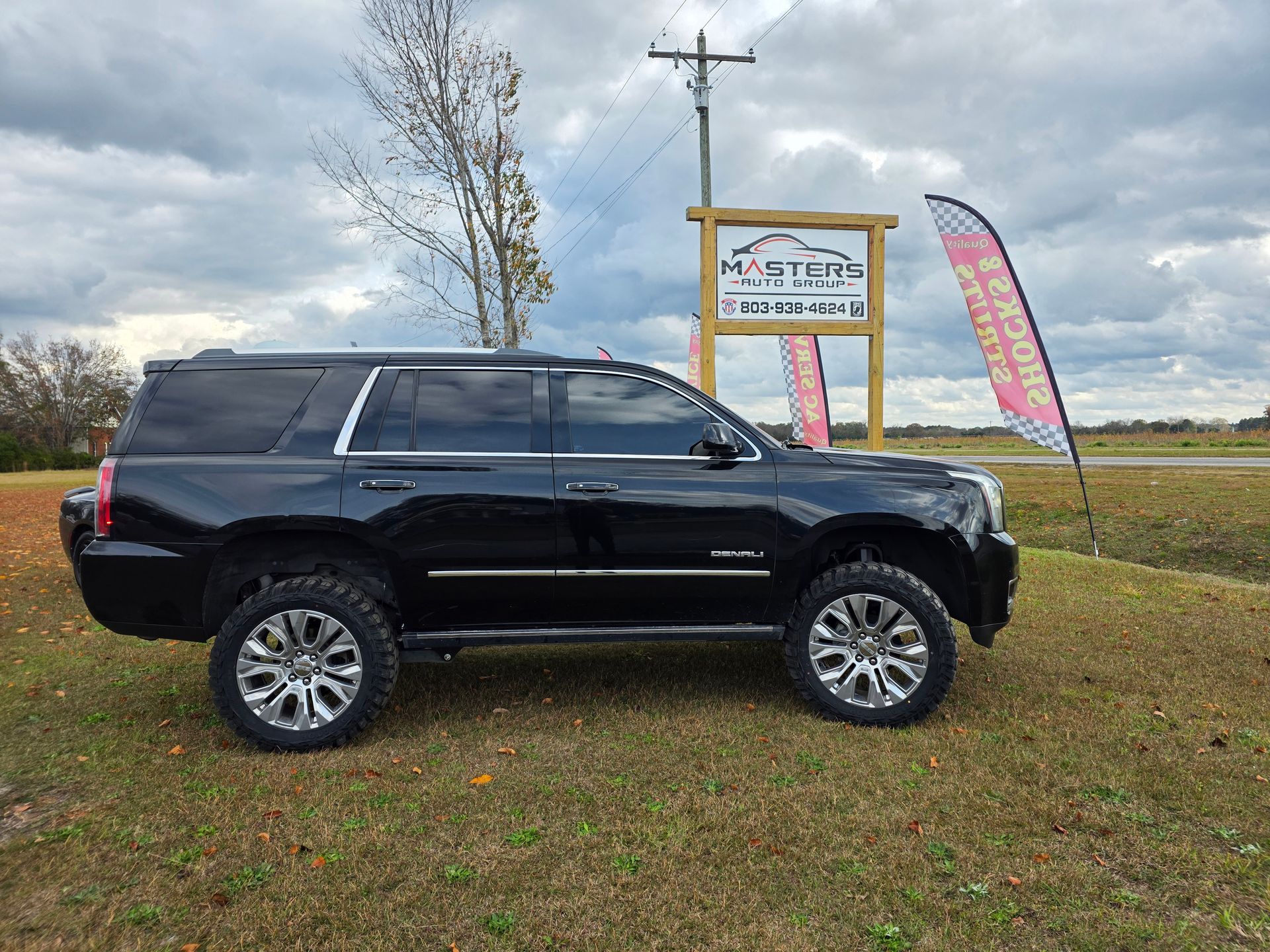 Black SUV parked on grass beside a roadside sign and colorful flags under a cloudy sky | Masters Auto Group