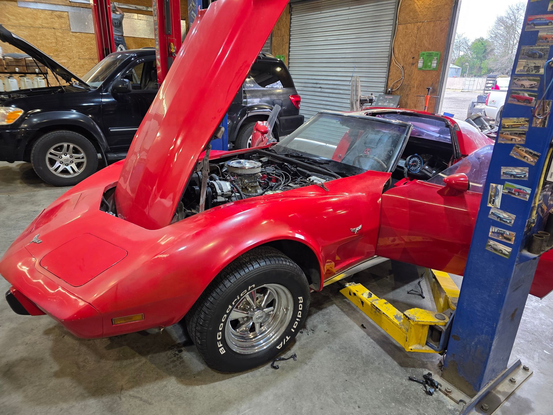 Red sports car with hood open in an auto repair shop, next to a blue lift and a black SUV | Masters Auto Group