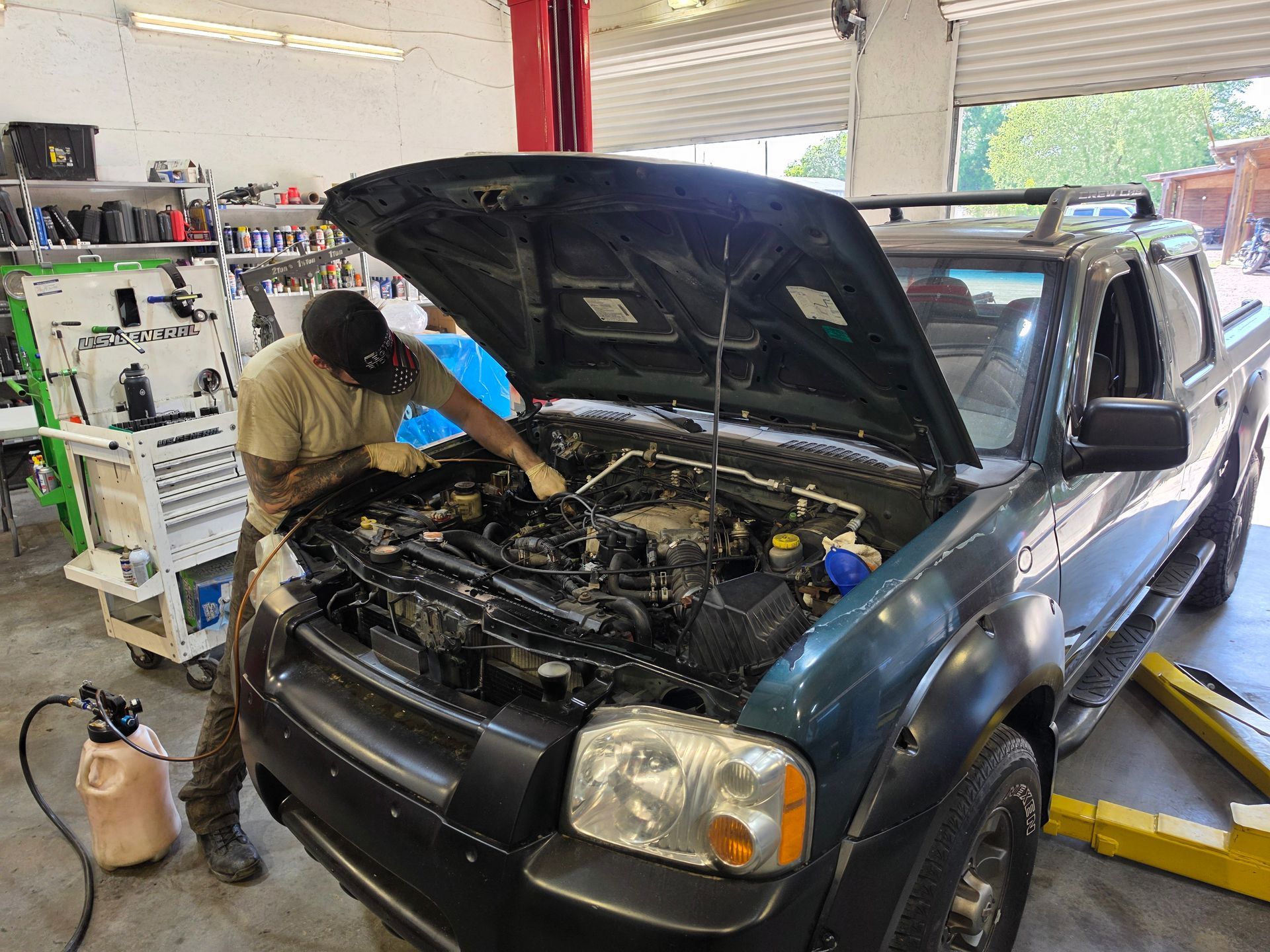 Mechanic working under the hood of a dark blue pickup truck in an auto shop | Masters Auto Group