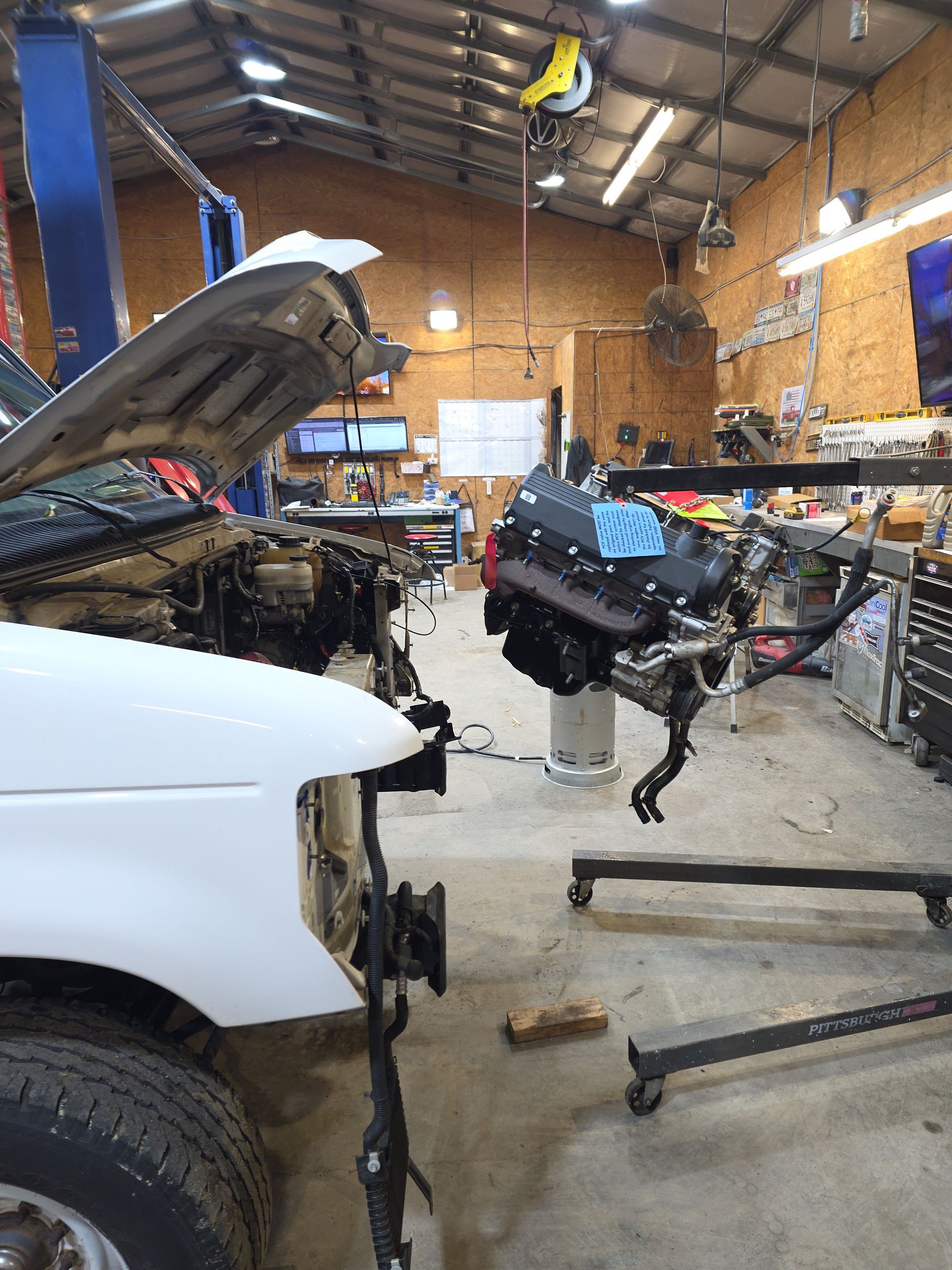 White car in a garage with its hood open during engine repair, engine hoist beside it | Masters Auto Group
