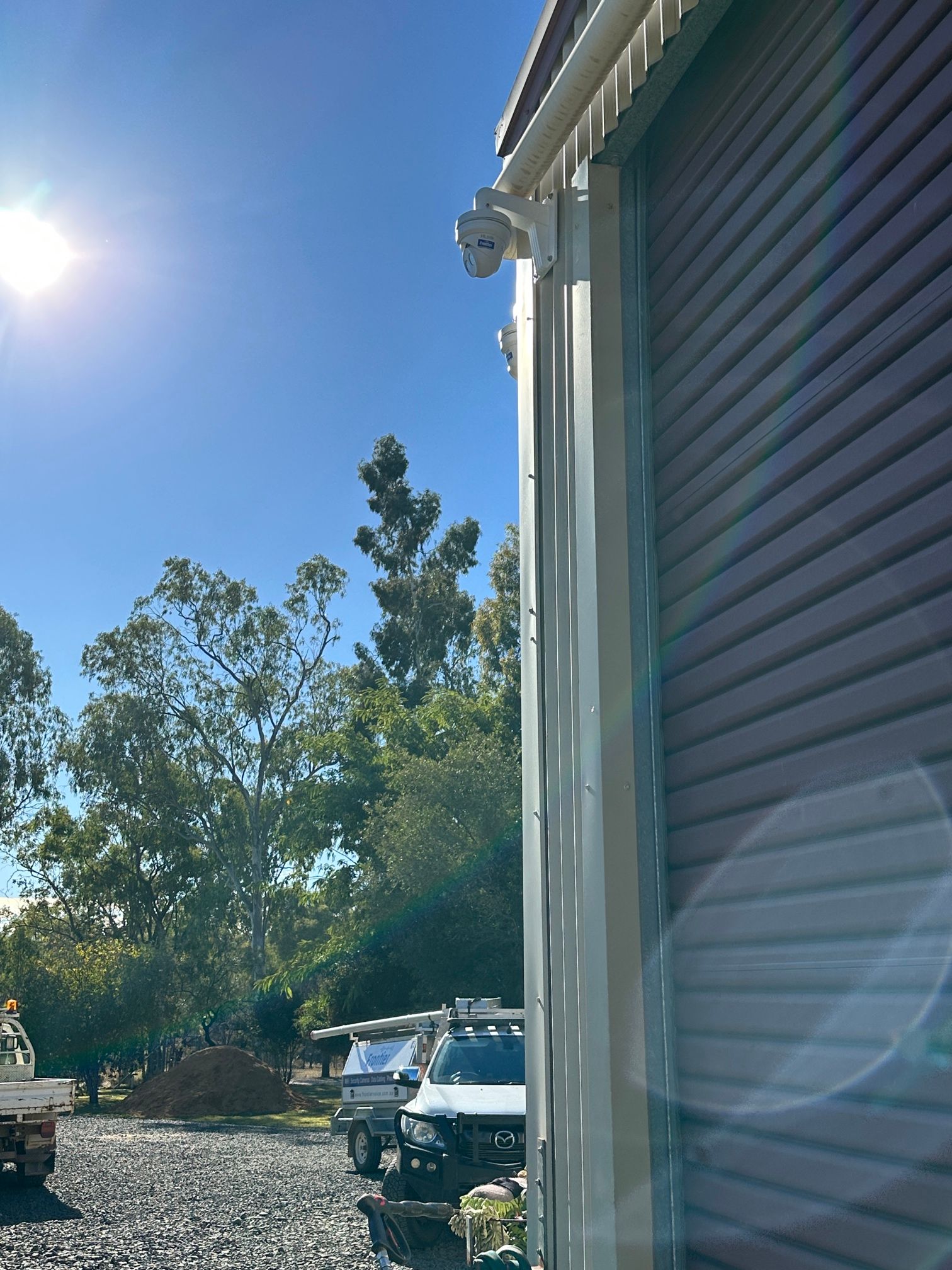 White Building With Security Camera Mounted on Corner, Parked Vehicles Below — Frontier Security in Chinchilla, QLD