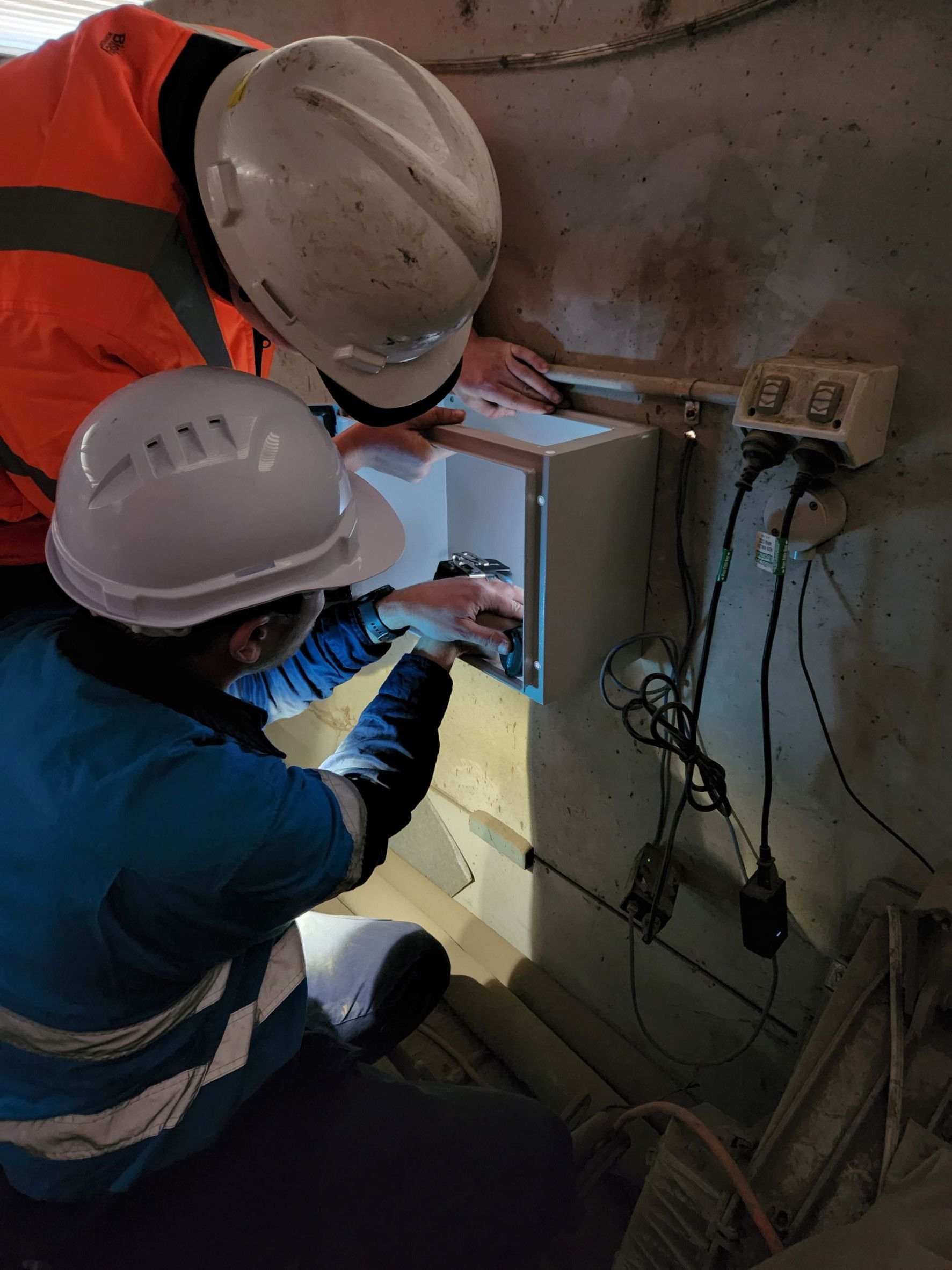 Two Construction Workers in Hard Hats Installing Electrical Equipment on a Concrete Wall — Frontier Security in Warwick, QLD 
