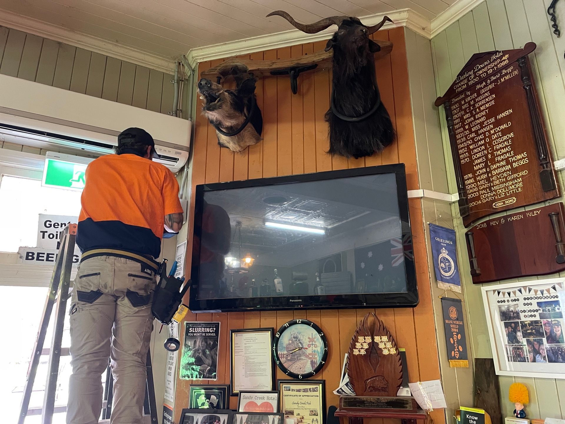 Man on Ladder Wiring Near a Mounted Tv and Animal Heads in a Wood-paneled Room — Frontier Security in Warwick, QLD 