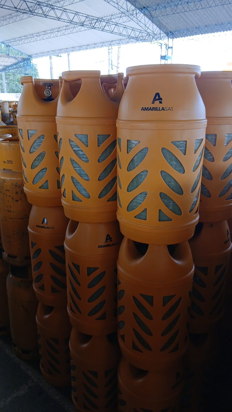 Cilindros de gas GLP naranjas apilados en un área de almacenamiento cubierta.
