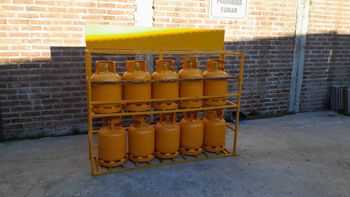 Cilindros de gas amarillos apilados en un estante metálico contra una pared de ladrillos al aire libre.