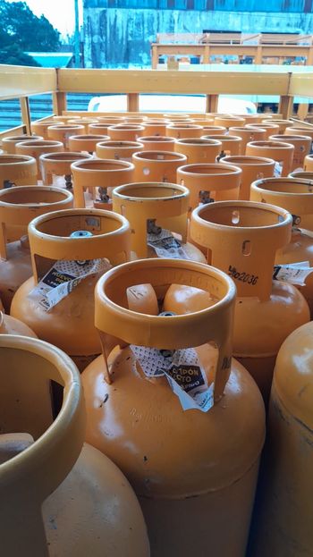 Filas de bombonas de gas de color naranja almacenadas al aire libre bajo un toldo, con un paisaje nevado de fondo.