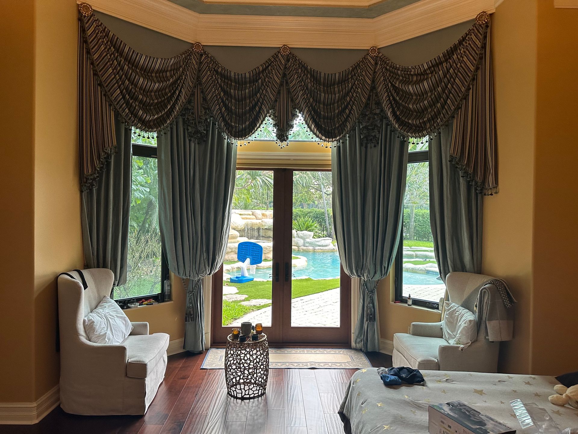 A bedroom with a bed , chairs , curtains and a view of a pool.
