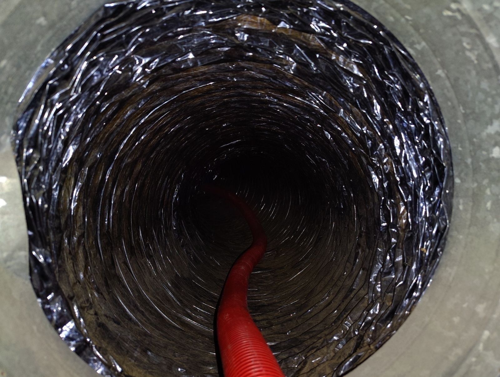 A red hose is going through a hole in a duct