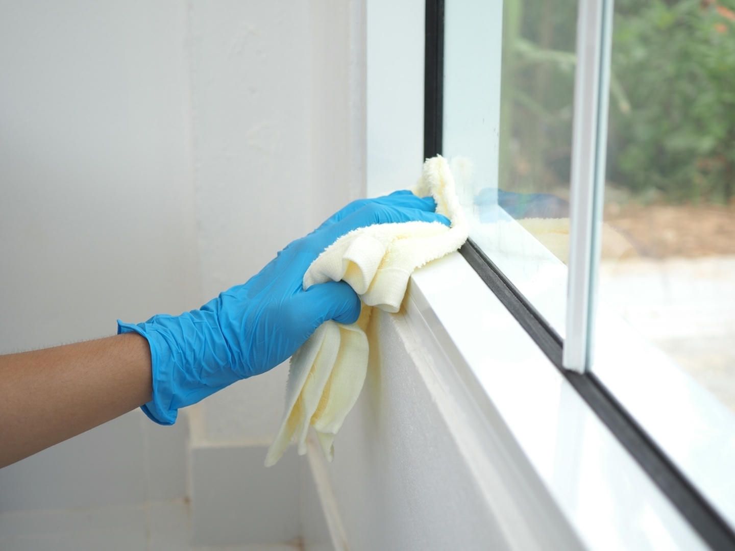 A person wearing blue gloves is cleaning a window with a cloth.