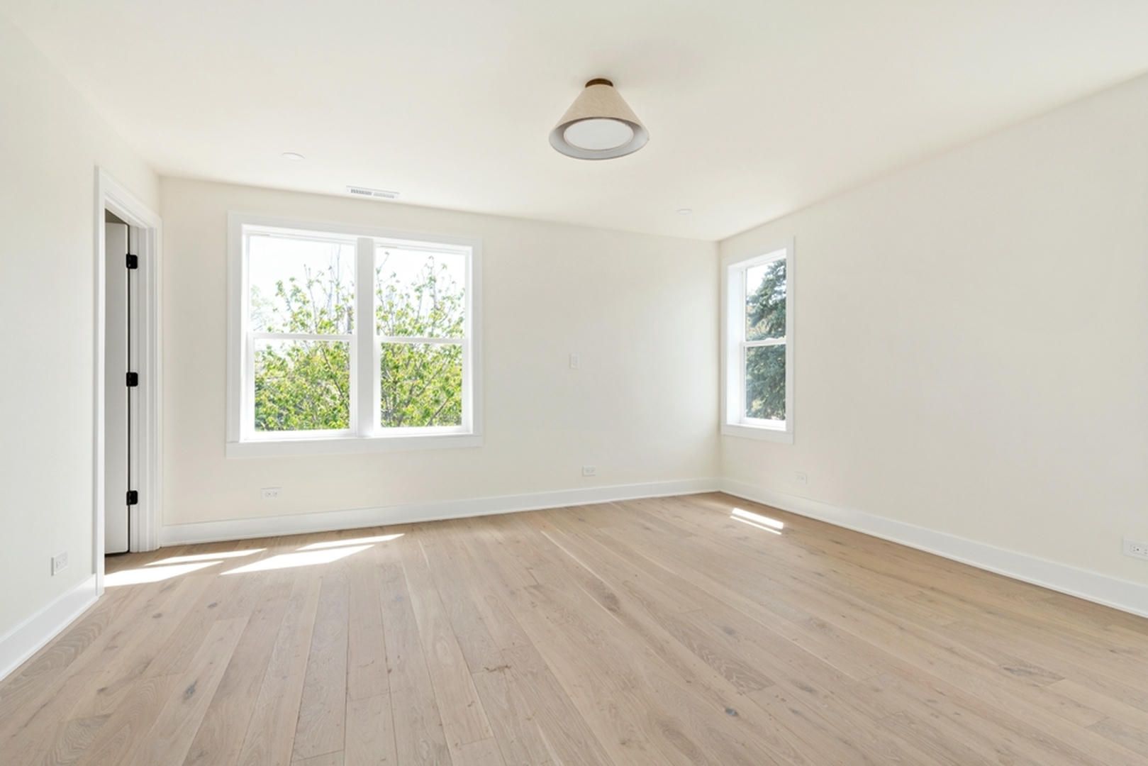 An empty room with hardwood floors and two windows.