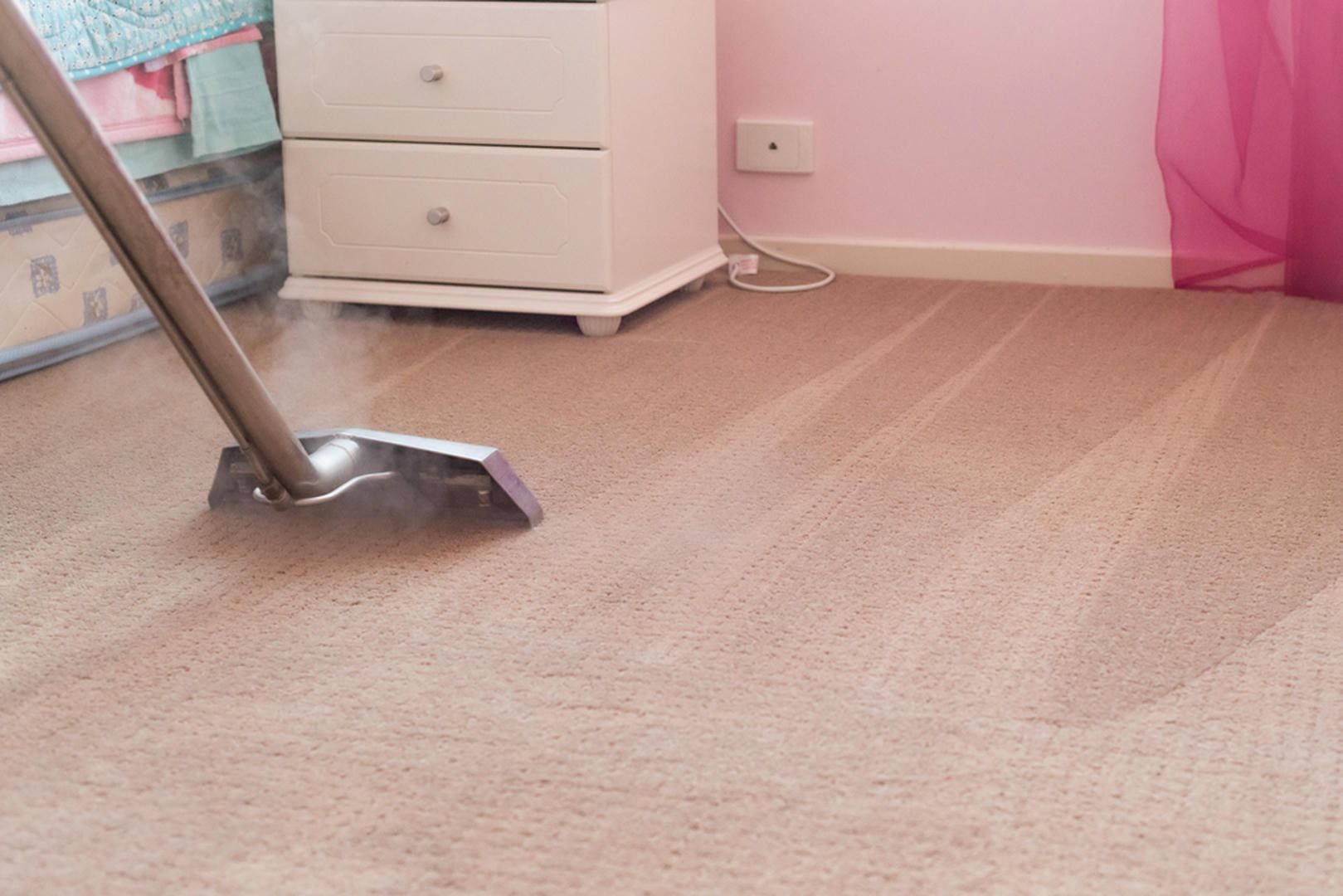 A vacuum cleaner is cleaning a carpet in a bedroom.