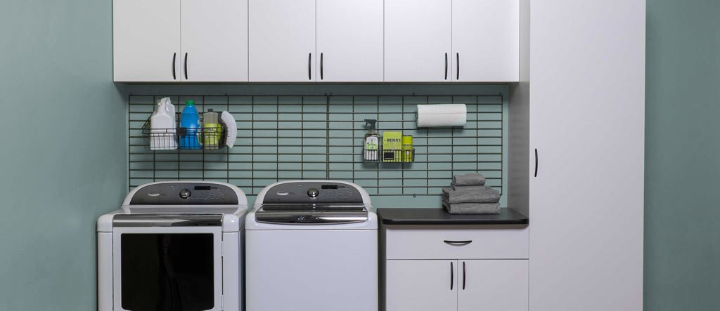 Small modern laundry room with washer, dryer, sink, and white cabinets on a tiled floor.