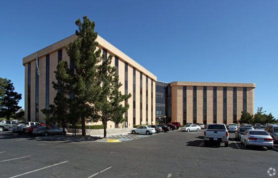 Office building with many parked cars in a large parking lot under a blue sky.