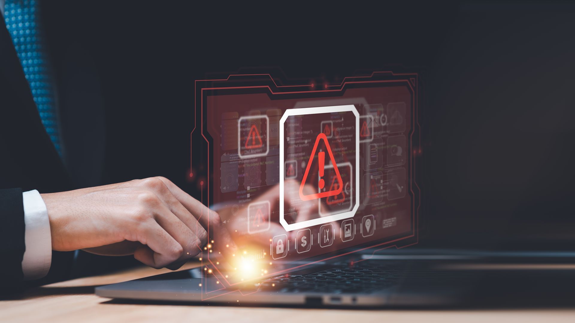 Hand using laptop with glowing red warning icon and cybersecurity interface overlay