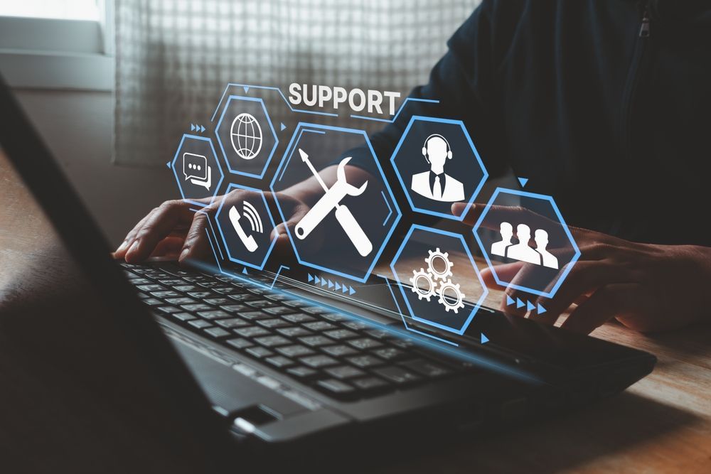Person using a laptop with digital support icons overlaid: global, chat, phone, tools, person, and teamwork.