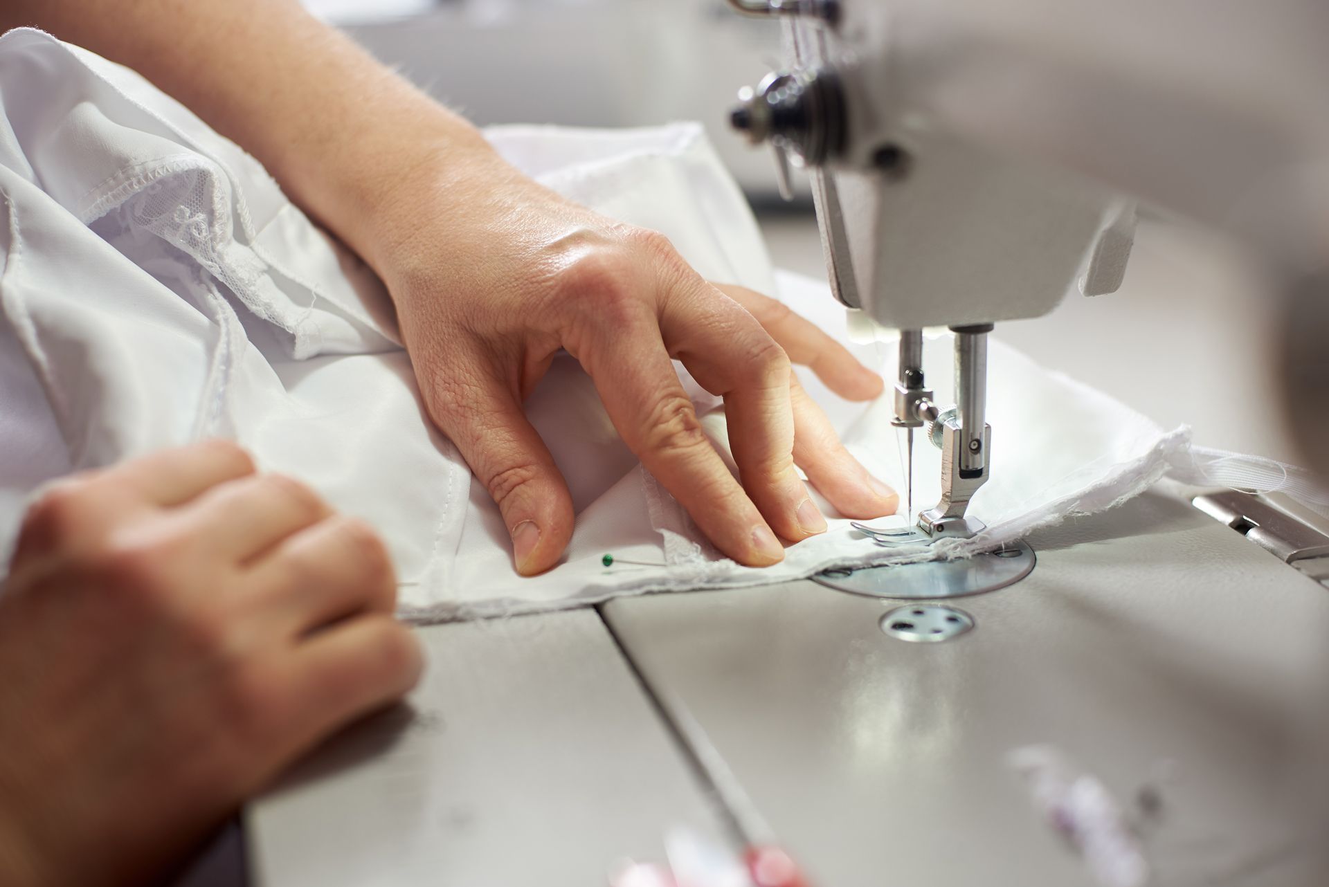 Hands guiding fabric under a sewing machine needle on a white sewing table